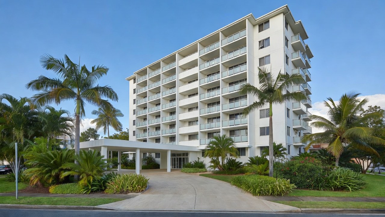 A white eight-storey apartment building with balconies and palm trees