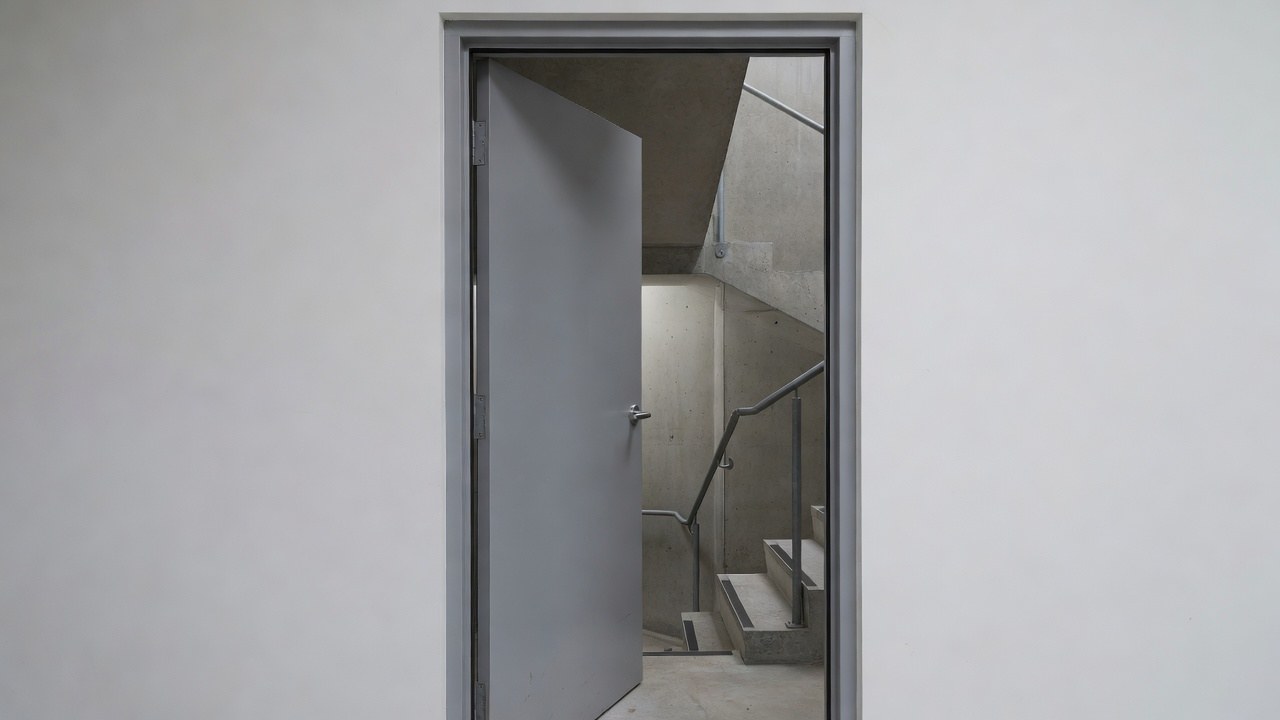 A grey steel-framed fire door standing half open into a concrete fire stair